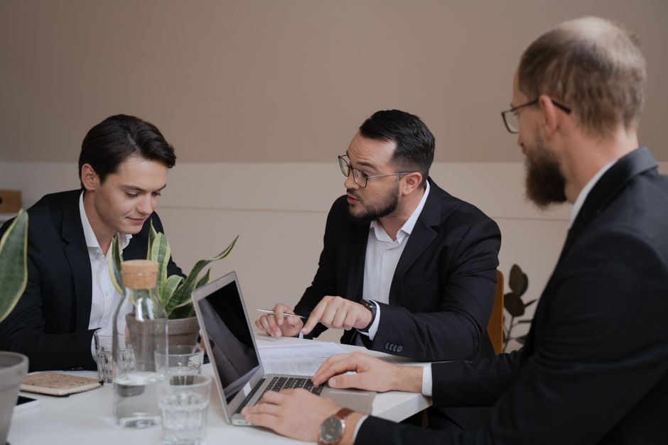 Un grupo de empresarios involucrados en una reunión, analizando informes y utilizando un portátil para su discusión.