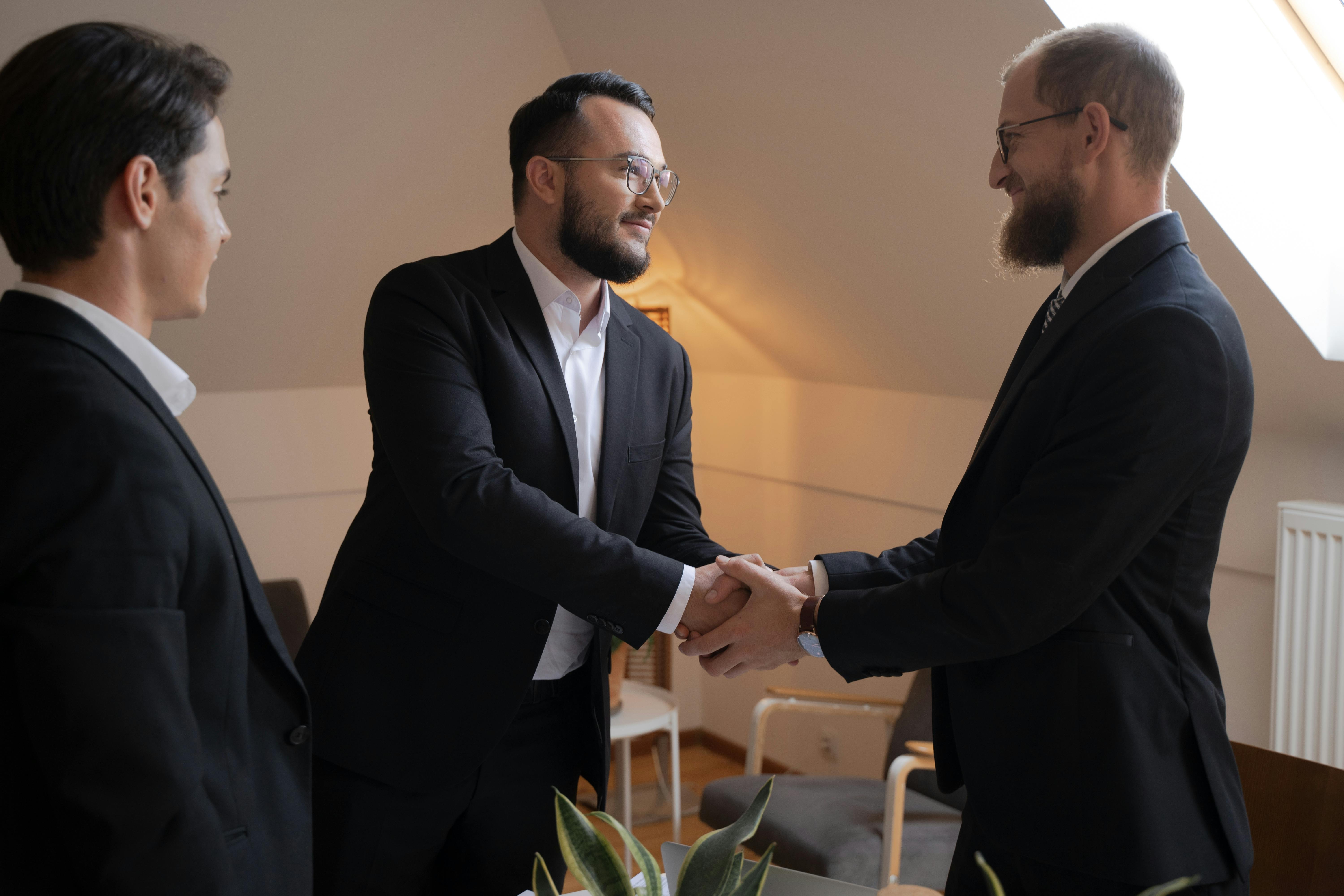 bearded men in black suit doing handshake while looking at each other