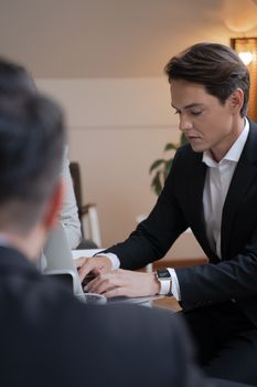 A serious businessman in a black suit intensely working on his laptop indoors.