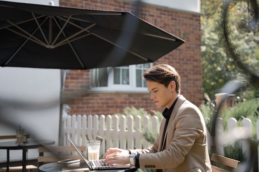 Businessman in a beige suit working on a laptop outdoors, showcasing modern technology use.