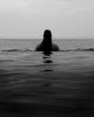 Black and white of anonymous dark haired female swimming in rippling sea against skyline