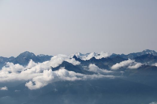 Majestic aerial view of Swiss Alps with clouds floating below mountain peaks in a clear sky.