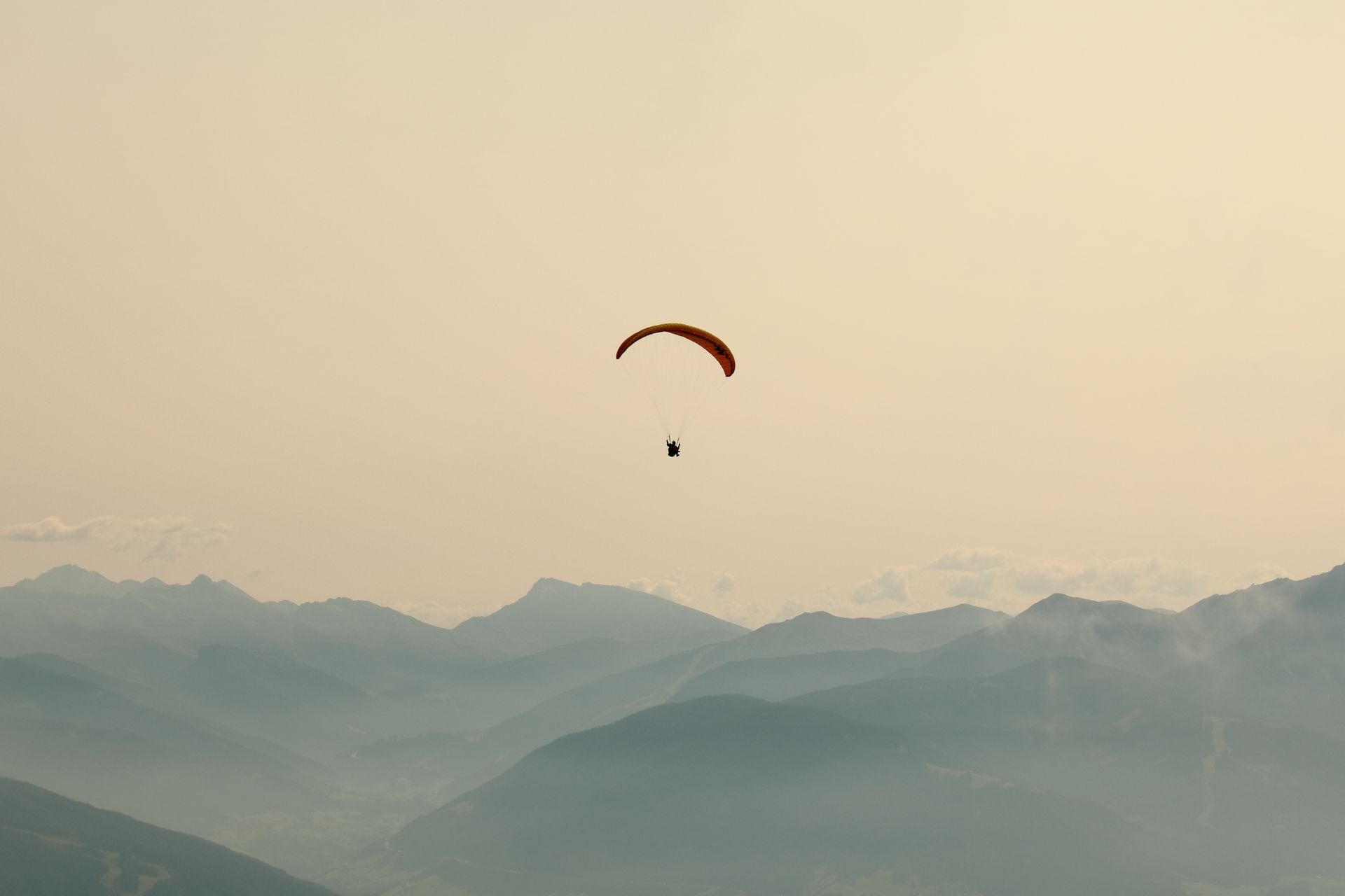 A paraglider soars over scenic mountains near Innsbruck, Austria, under a clear sky.