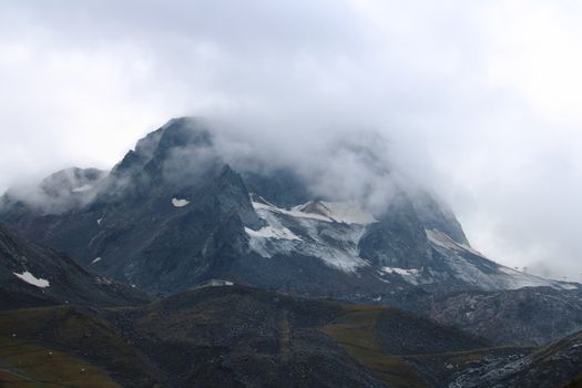 Misty view of rugged mountain peaks in the Swiss Alps, with snow and clouds covering the landscape.