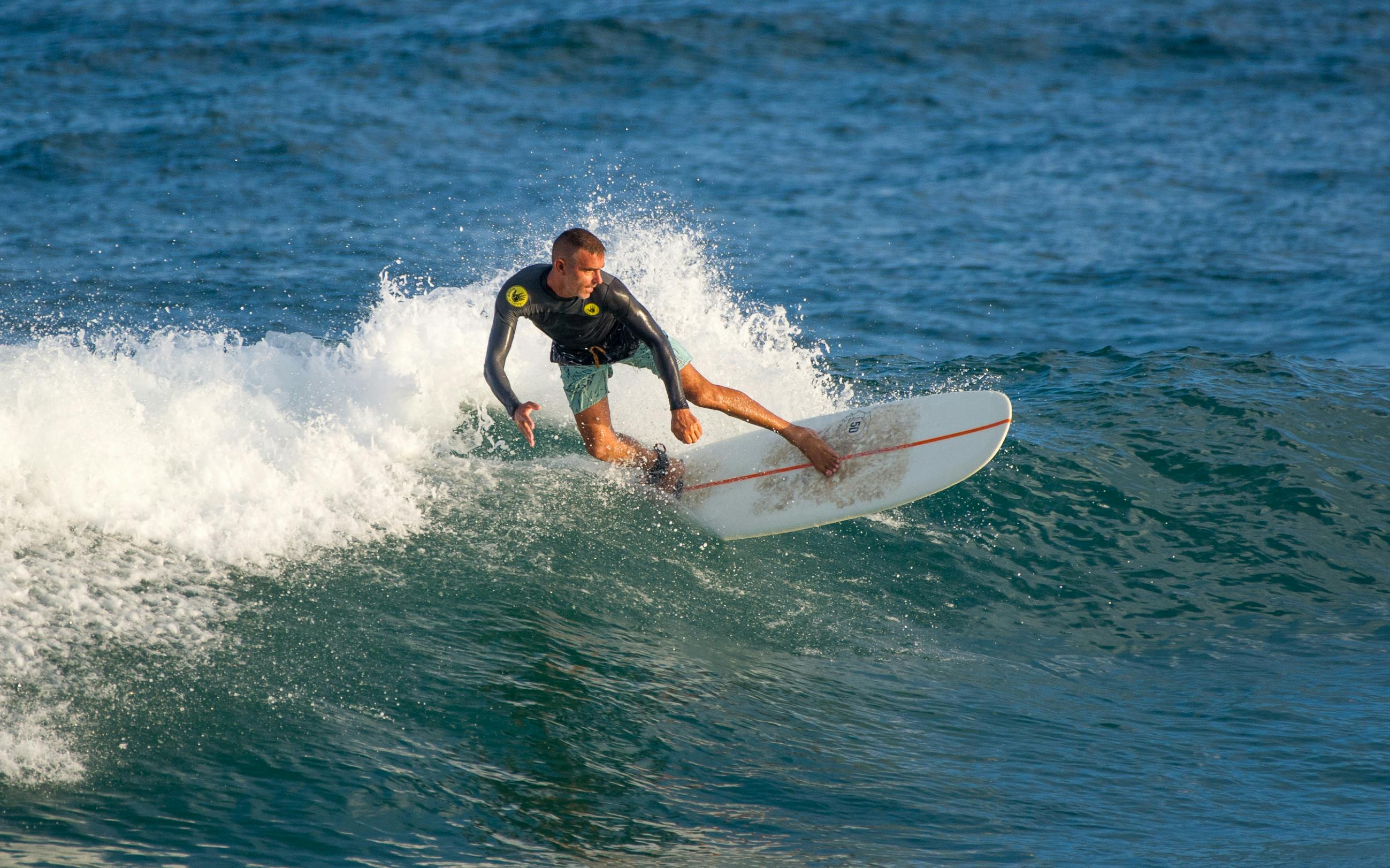 A skilled surfer expertly rides the ocean waves under clear skies, showcasing surfing prowess and balance.