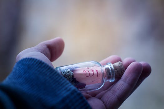 Macro shot of a hand holding a glass bottle with cork lid, containing an object and text.