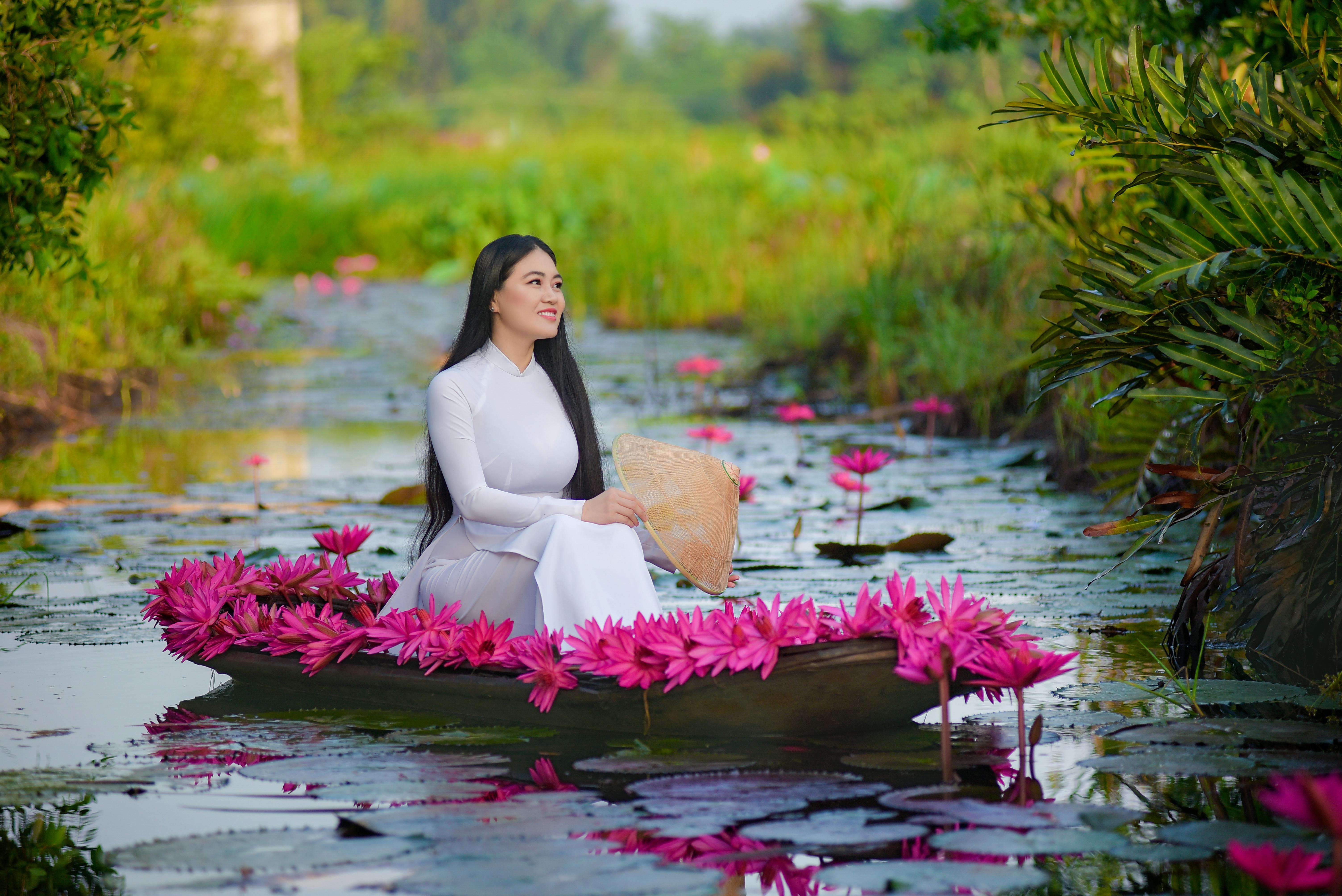 beautiful woman in a white dress sitting on a boat with pink water lilies