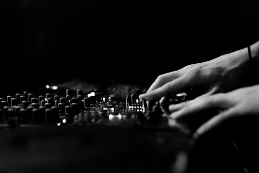 Artistic black and white image of hands adjusting a DJ console in a club.