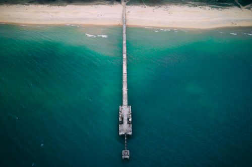 Free Drone view of long pier near sandy shore washed by turquoise water of blue endless ocean Stock Photo