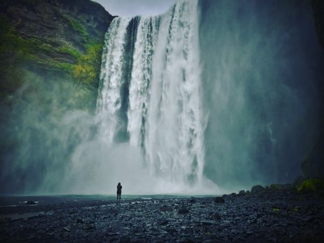 Person admiring the powerful Skógafoss waterfall in Iceland, surrounded by nature's beauty.