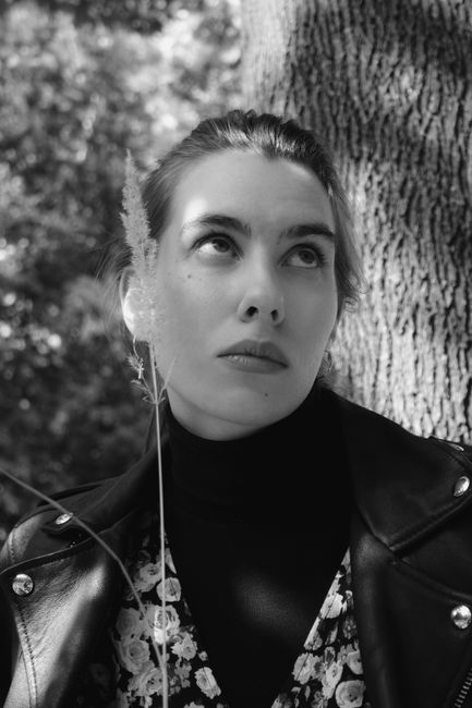 Black and white of young contemplative lady with makeup and dry sprig in trendy clothes looking up near tree