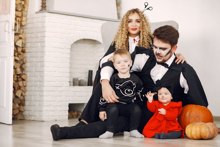 Family In Halloween Costumes Sitting By The Fireplace