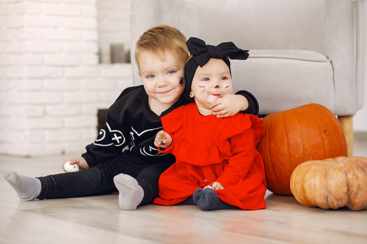 Two toddlers in Halloween costumes sitting and playing with pumpkins