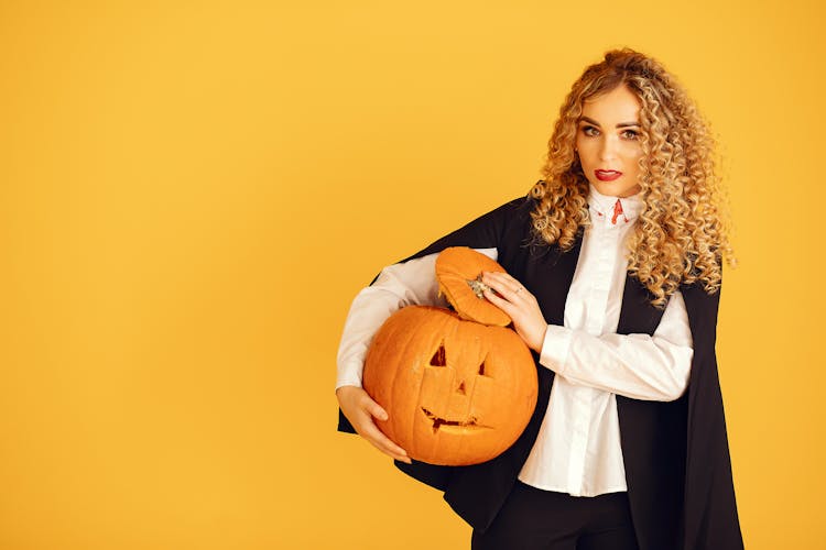 A Woman With Curly Hair Holding A Carved Pumpkin