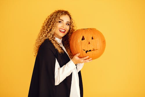 Smiling Woman in Black Coat Holding Pumpkin