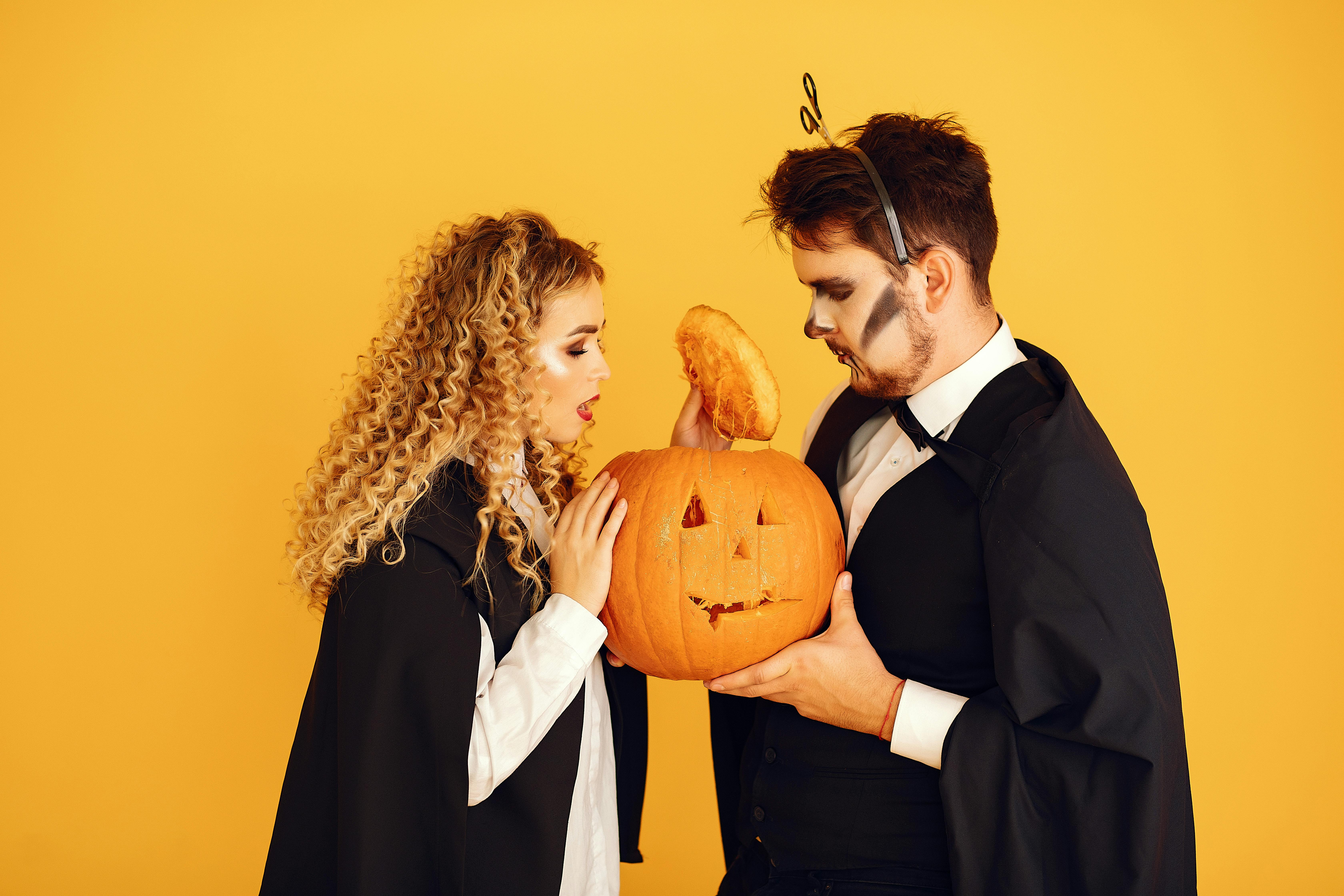 man in black suit and woman holding jack o lantern and opening its head