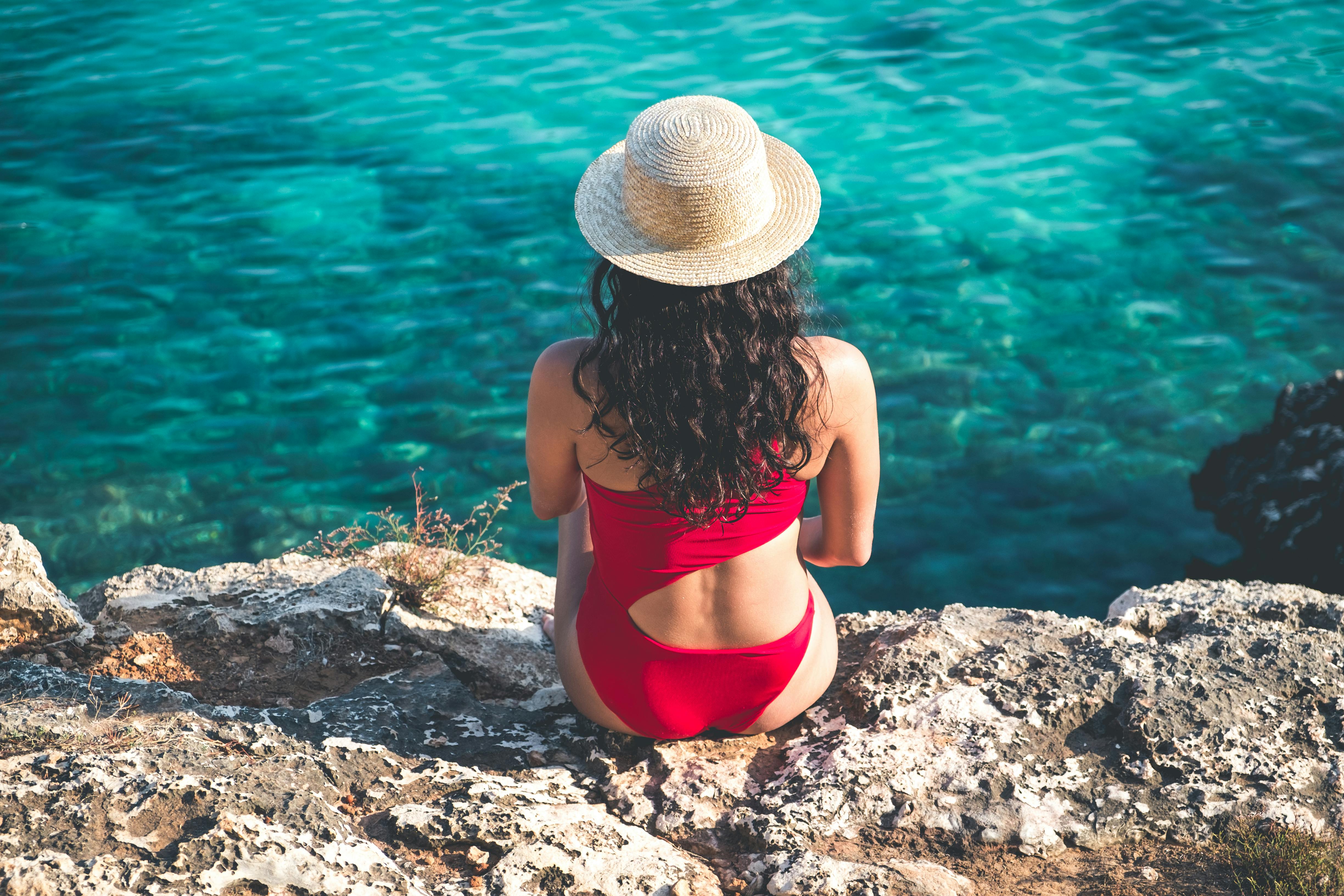 Free A woman in a red bikini and straw hat relaxing by the turquoise sea. Stock Photo