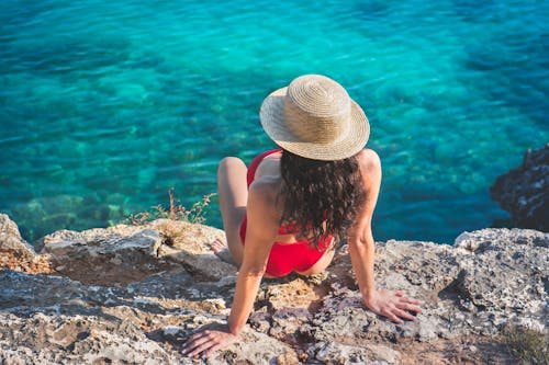 Woman in Red Bikini Wearing Straw Hat Sitting on Rock Near Water