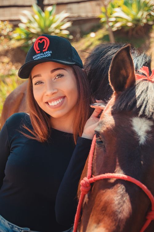 Free Young woman smiling next to a horse in a sunny outdoor setting, enjoying nature. Stock Photo