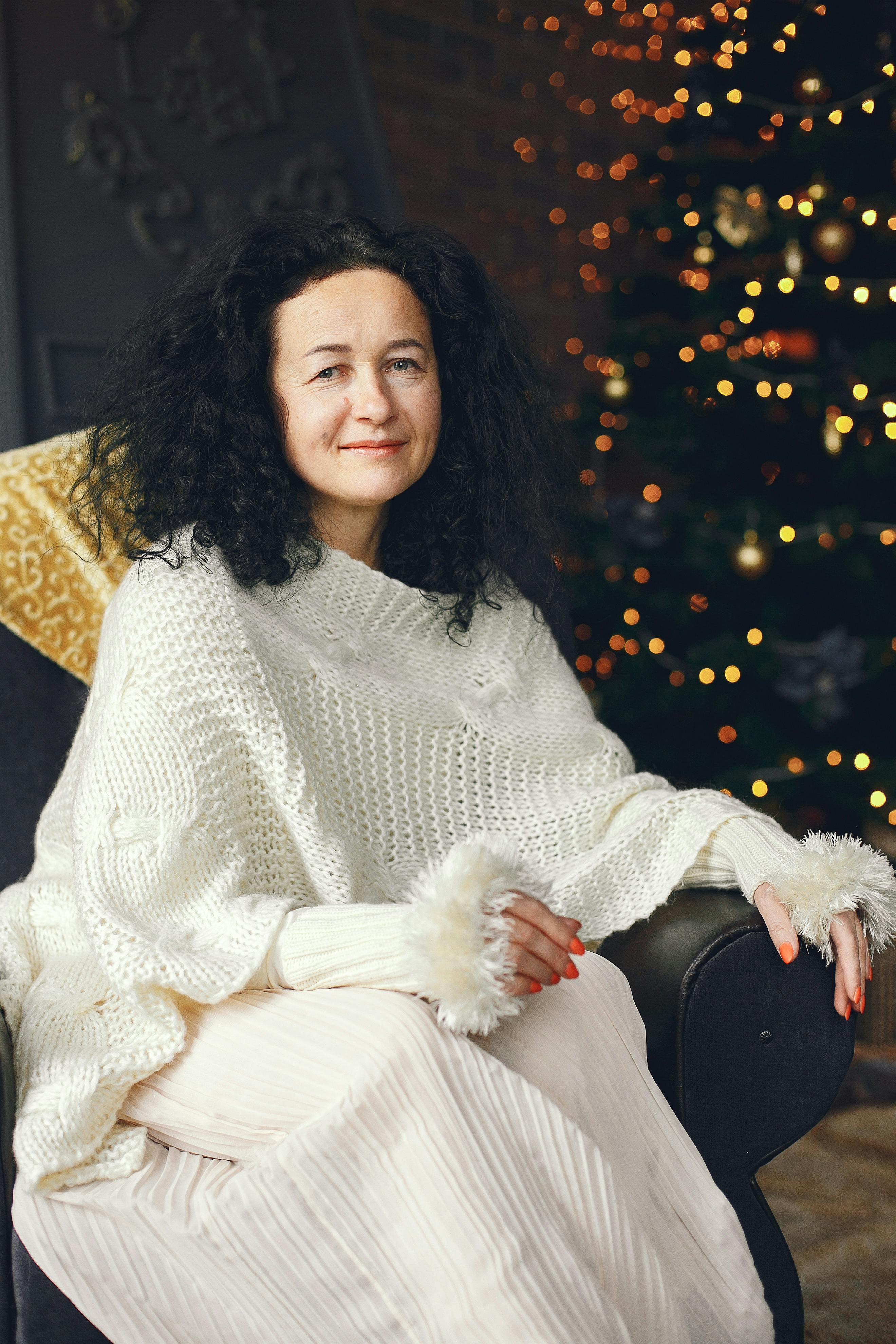 Cozy winter portrait of a woman seated by a Christmas tree indoors.