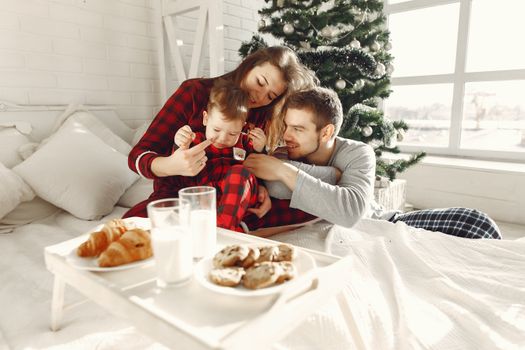 A loving family enjoys breakfast in bed next to a beautifully decorated Christmas tree.