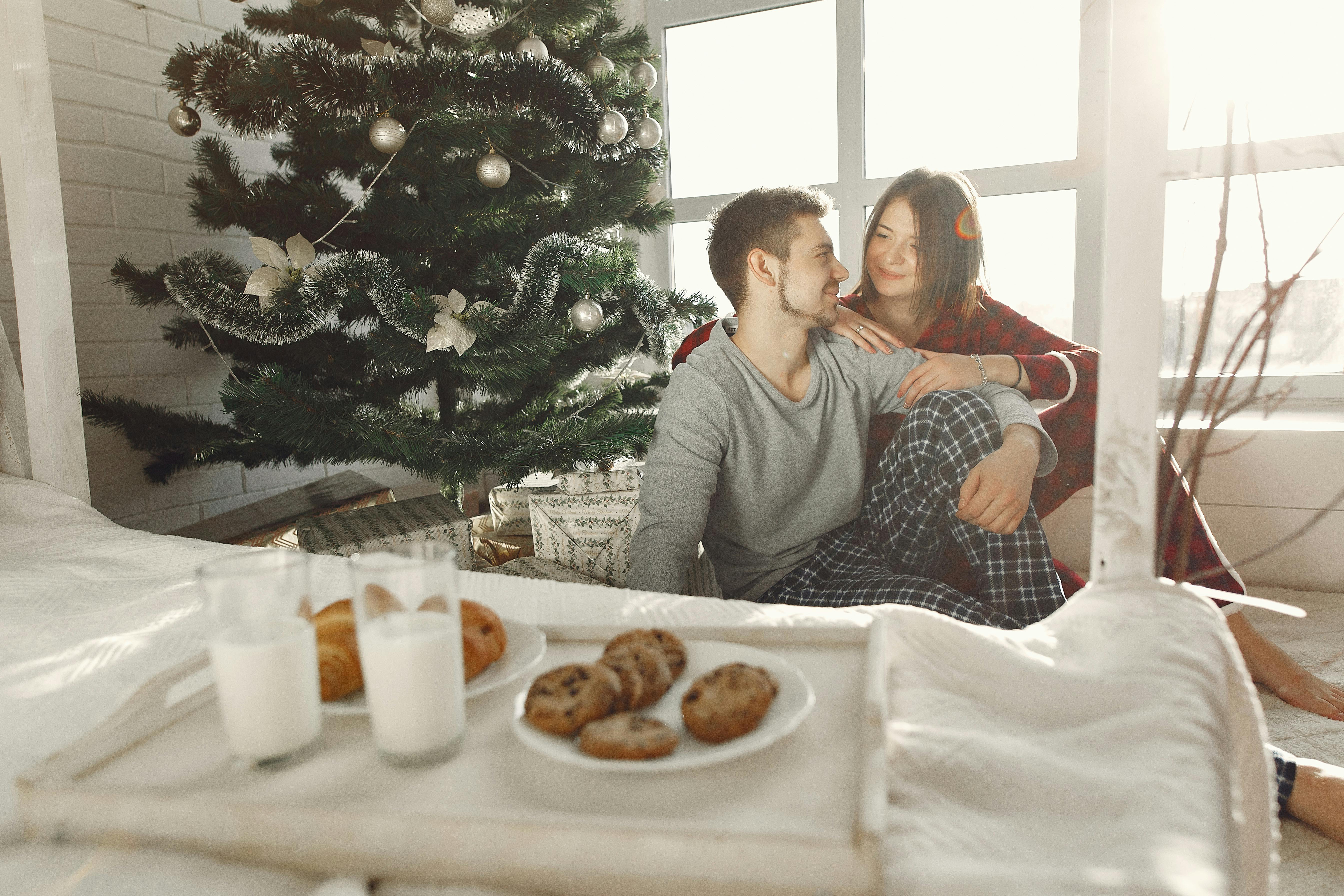 A couple enjoys a cozy morning by the Christmas tree with milk and cookies, capturing holiday warmth.