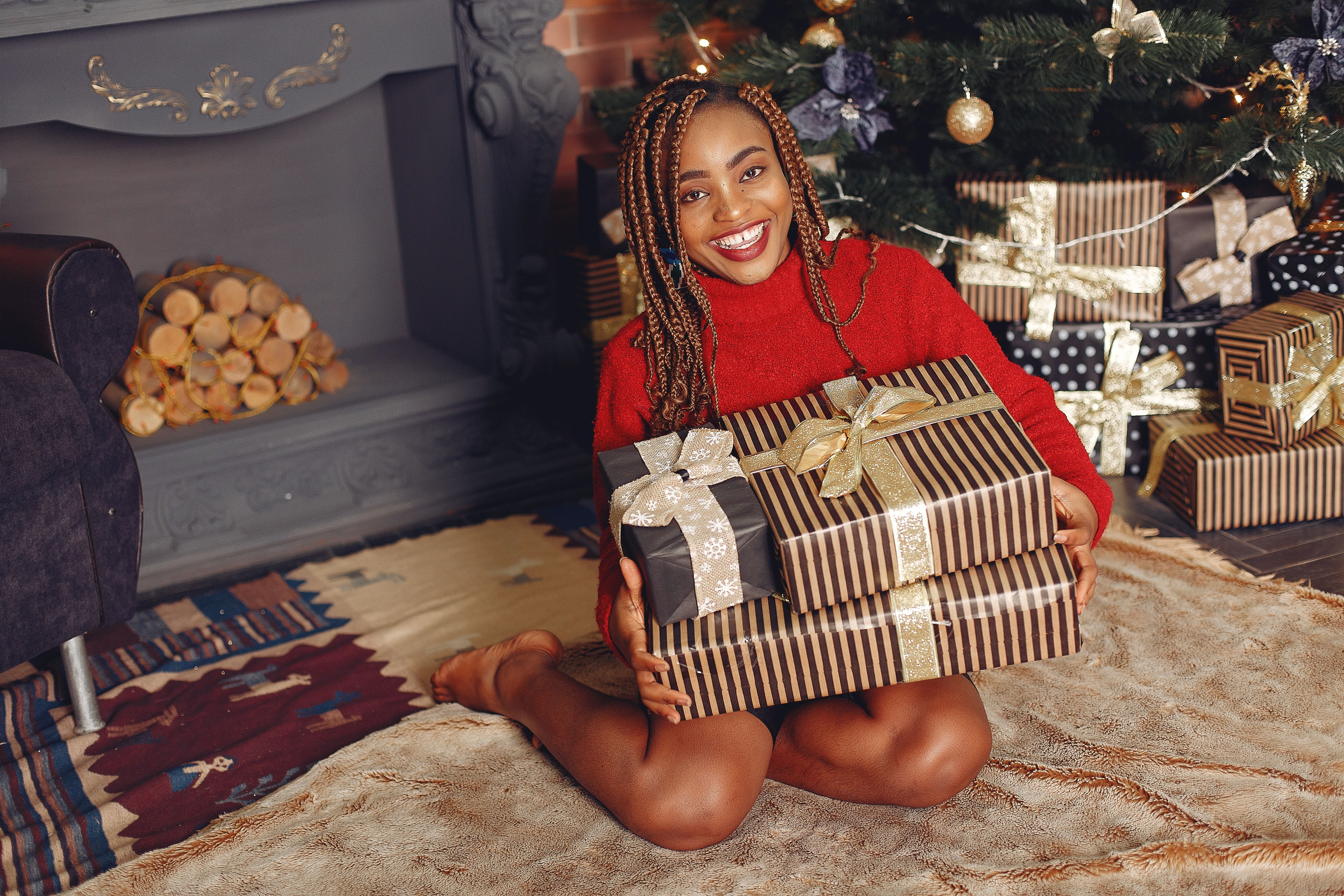 Smiling woman in red sweater with gifts by the fireplace and Christmas tree.