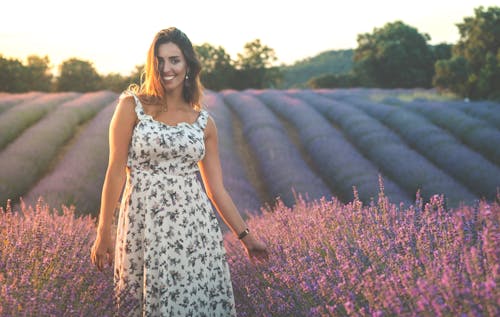 Free A Woman in White and Black Sleeveless Dress Standing on Purple Flower Field Stock Photo