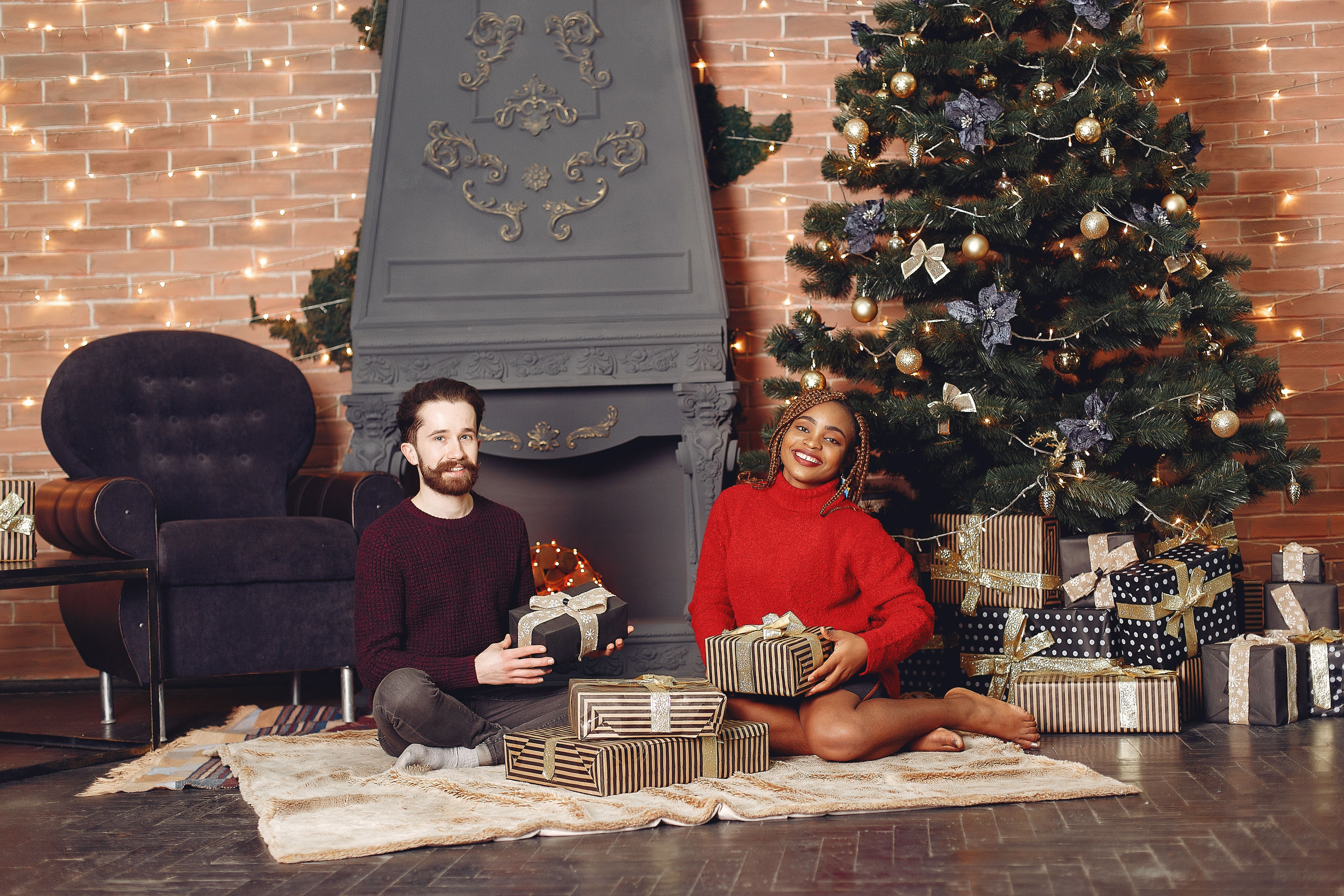 A joyful couple exchanging Christmas gifts by a decorated tree inside a festive living room.
