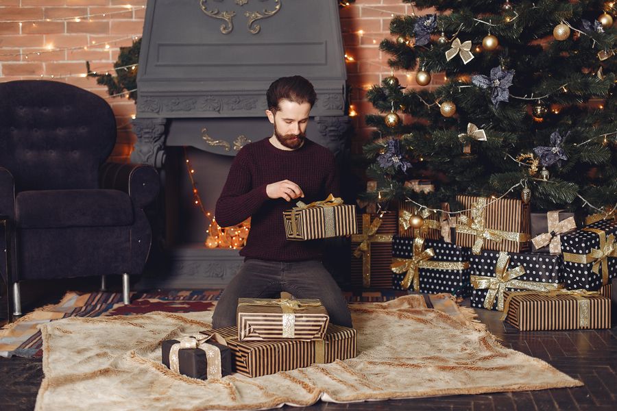 Homme entouré de cadeaux emballés près d'un sapin et d'une cheminée