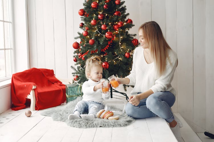 Woman And Child Drinking Juice Beside A Christmas Tree