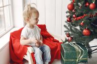 Boy in Red Crew Neck T-shirt Sitting on Green Box Beside Green Christmas Tree