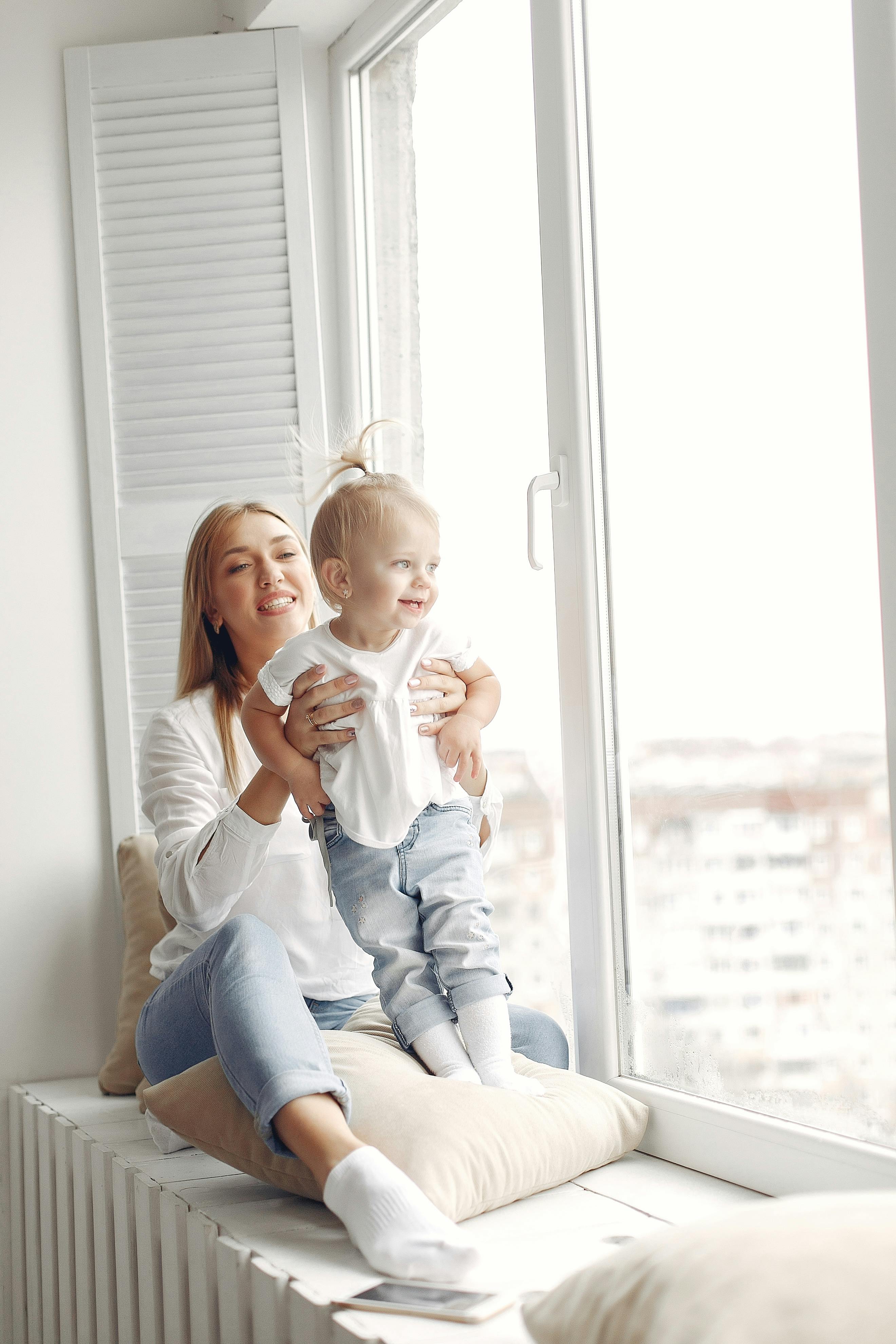 happy mother and daughter sitting on a windowsill