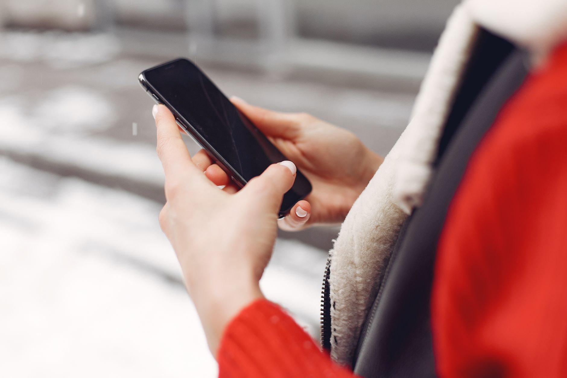 mengatasi broken link - Close-up of hands holding a smartphone in winter, wearing a red coat.