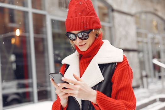 Stylish woman in red winter clothing using smartphone on a snowy street.