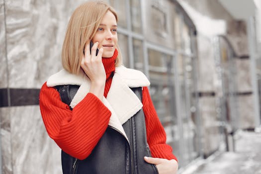 Woman in a vibrant red sweater and black vest talking on the phone outdoors.