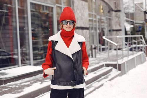 Free A stylish woman in a red beanie and leather jacket poses confidently on a snowy city sidewalk. Stock Photo