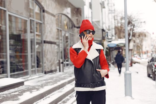 Fashionable woman in winter clothes having a phone conversation on a snowy city street.