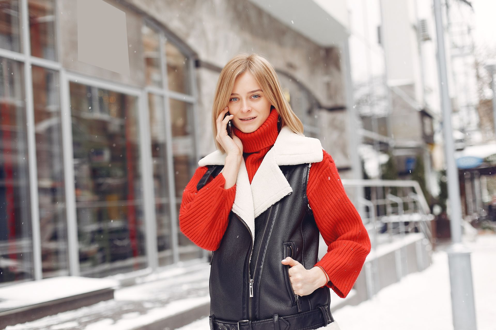 Young woman wearing winter clothing making a phone call outside in snowy urban area.