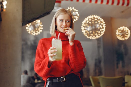 Woman in red sweater sipping a juice inside a decorated, warm-lit cafe.