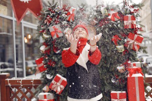 Free A woman joyfully plays in the snow with Christmas decorations creating a festive atmosphere. Stock Photo