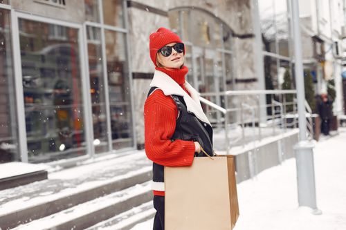 Free Woman in winter attire holding shopping bags in snowy urban setting. Stock Photo