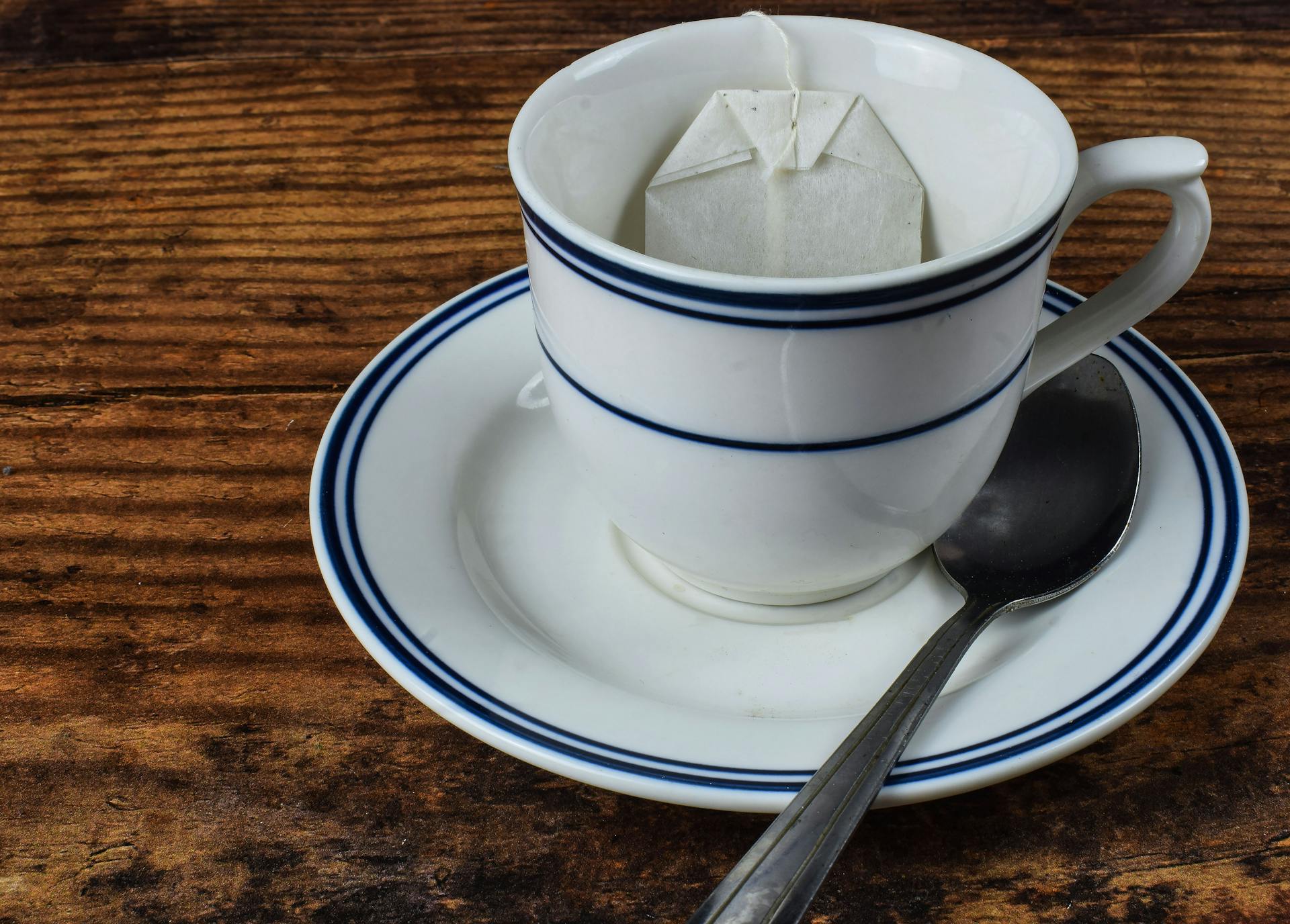 Close-up shot of a teacup with a tea bag and spoon on a wooden table, perfect for food and beverage themes.