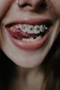 Crop female with metal braces on upper teeth and nose piercing smiling coquettishly and showing tongue