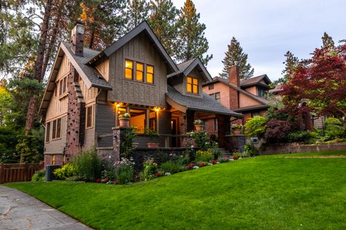Free A beautifully lit Victorian-style house surrounded by a lush garden at twilight, showcasing classic architecture. Stock Photo
