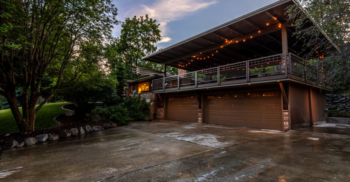 Spacious modern home's exterior with string lights illuminating a twilight setting, featuring lush greenery.