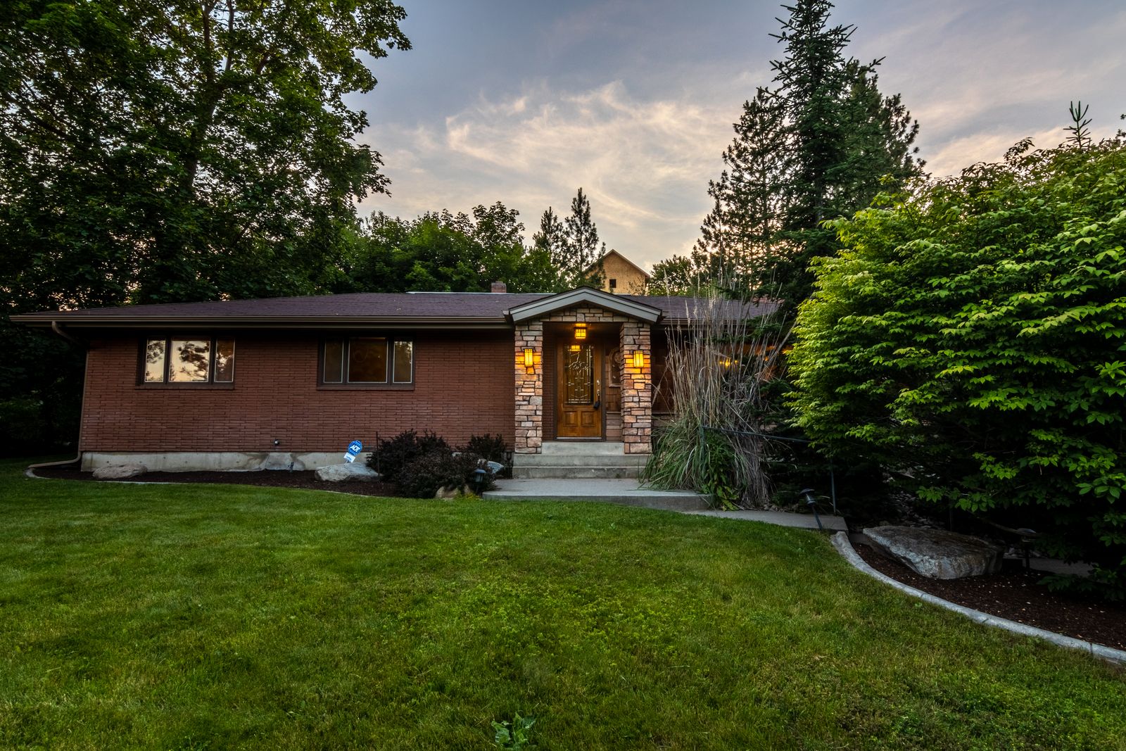 Single-story brick ranch home with a covered stone entry, lit at dusk and framed by mature green trees, Aero Estates, Naperville IL
