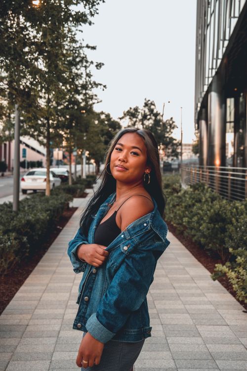 Free Young woman in a denim jacket posing confidently on a city sidewalk, exuding style and charisma. Stock Photo