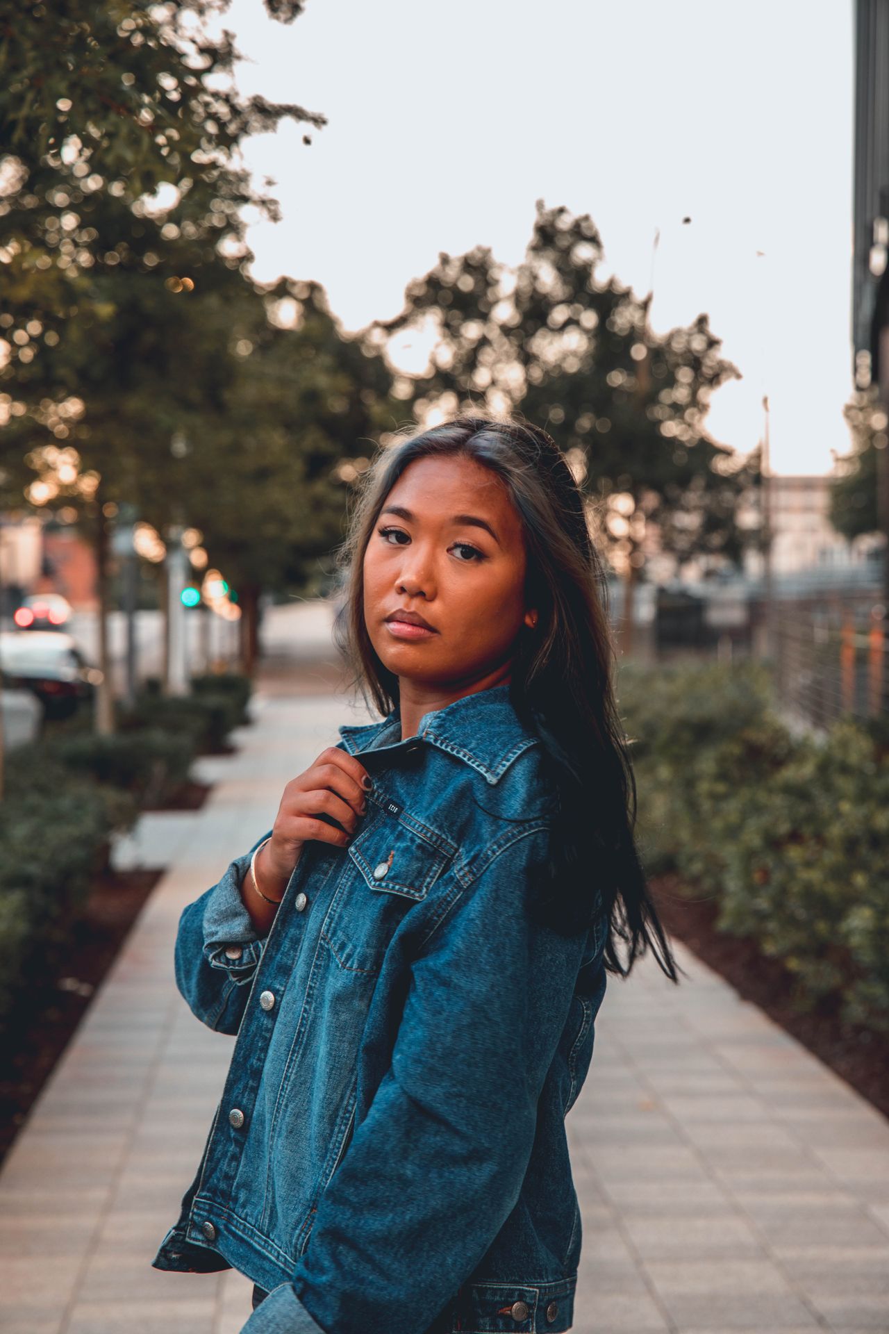 Young woman in a denim jacket on a city sidewalk at dusk
