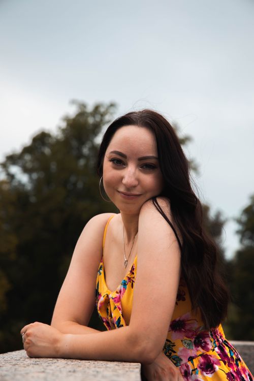 Free Portrait of a smiling woman wearing a floral dress outdoors against a natural background. Stock Photo